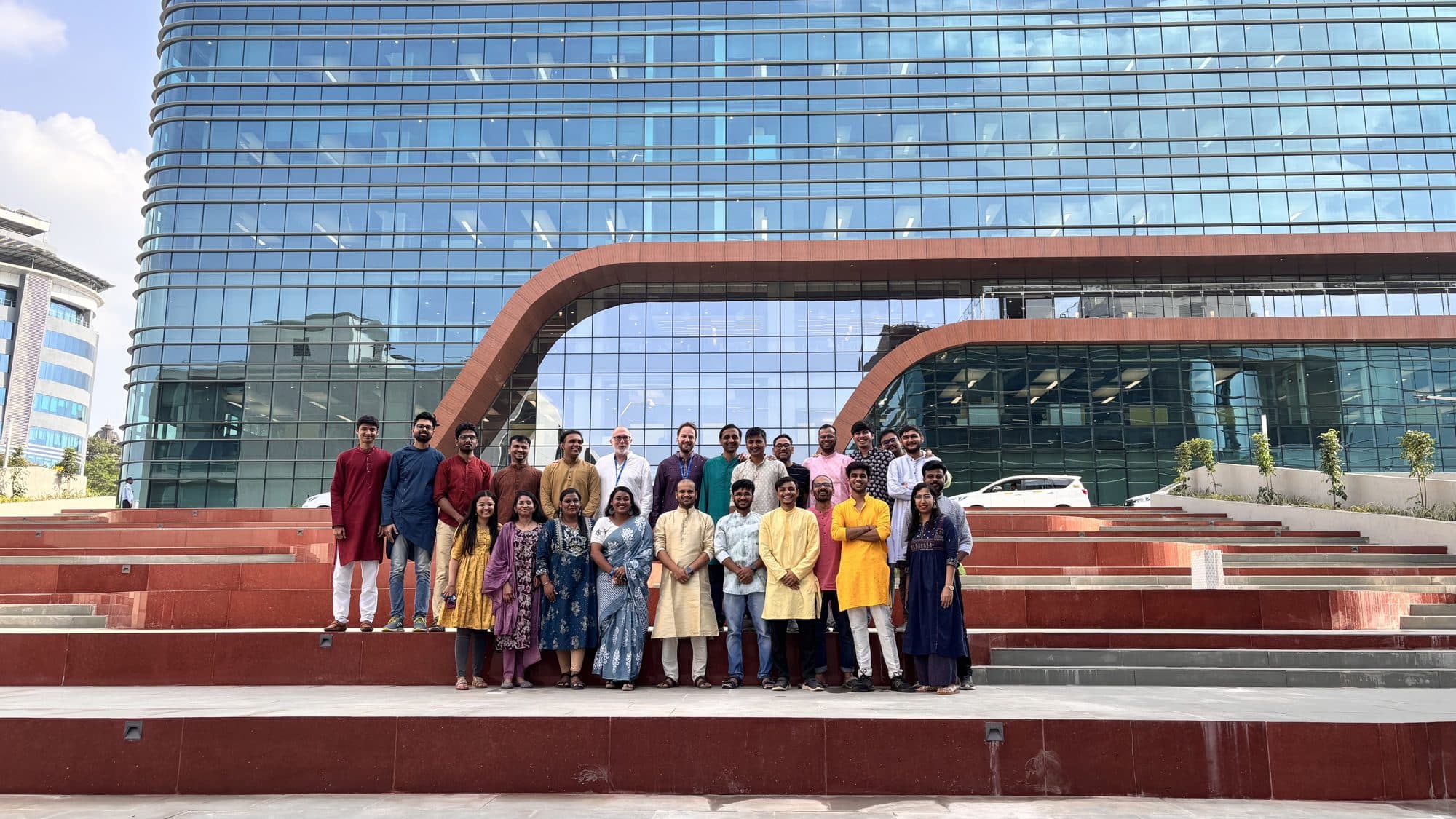 The team standing on red steps in front of the glass Dassault Systèmes building in Pune