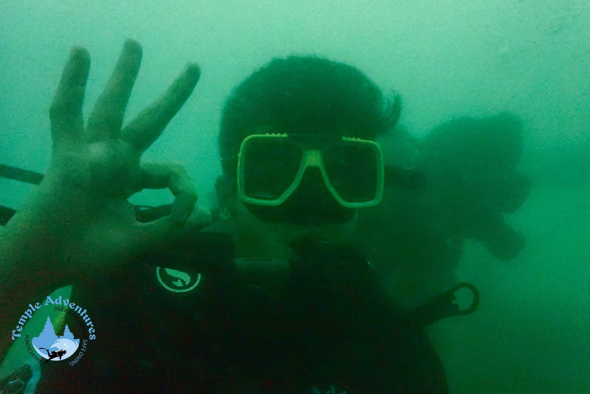 Underwater in scuba gear, making the OK sign